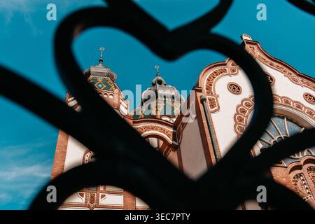 Sinagoga di Subotica vista attraverso una recinzione decorativa in ferro a Subotica, Serbia. Vista artistica dello storico monumento Art Nouveau con dettagli decorati. Foto Stock