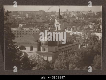 Cattedrale. Vista generale; fotografia intitolata Vilnius, volume 1, Bułhak, Jan 1876–1950, panorama di Vilnius, 1912; fotografia, stampa fotografica: altezza 10,5 cm, larghezza 15,7 cm; pagina album: altezza 31,0 cm, larghezza 23,5 cm., l'immagine mostra una vista aerea di un paesaggio urbano con un grande edificio classico in primo piano caratterizzato da una cupola prominente e un'alta torre sormontata da una guglia, fiancheggiata da statue sul tetto; l'edificio ha un esterno chiaro e un tetto cupola più scuro. Intorno all'edificio principale ci sono alberi e fogliame nella parte inferiore dell'immagine e un denso gruppo di tetti e Foto Stock