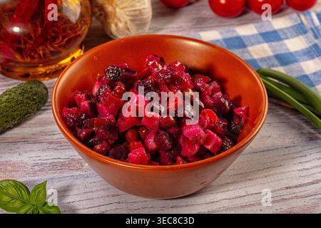 Primo piano con tradizionale insalata di vinaigrette. Barbabietole, patate e verdure tagliate a dadini in un recipiente marrone su un tavolo rustico in legno. Ingredienti freschi e a scacchi Foto Stock