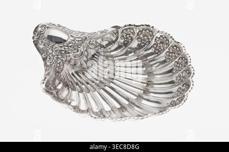 Piatto d'argento a forma di conchiglia di Atkin Brothers Silversmith Ltd Sheffield; azienda orafa e argentiera; 1826–1958, 1893–1894. Vaso a forma di capesante che termina su un lato con un manico stretto ovale e chiusura radiale; decorato sul bordo con ornamenti floreali in rilievo, volute e rotoli di acanto; sostenuto su tre piedini del guscio. Ornamenti floreali; foglie di acanto; decorazioni in rilievo. Altezza 5 cm, profondità 23 cm, larghezza 28,5 cm, larghezza alternativa 10 cm, peso 357 g., piatto in metallo decorativo a forma di conchiglia con dettagli floreali e a scorrimento rialzati ornati e una superficie argentata altamente riflettente, che mostra una Foto Stock