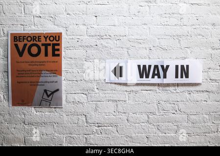 Prima di votare il poster informativo e il cartello con la freccia su un muro di mattoni in un polling station del Regno Unito, che ricorda agli elettori i requisiti per il documento di identità con foto di cui al punto Foto Stock