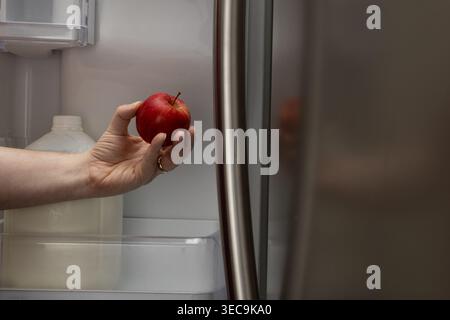Primo piano orizzontale di mano che prende la mela rossa da Refrigerator at Home Foto Stock