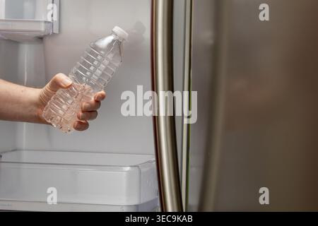 Primo piano orizzontale della mano che preleva una bottiglia d'acqua dal frigorifero a casa Foto Stock