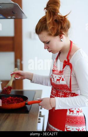Giovane donna dai capelli rossi che cucina il piatto di barbabietole in cucina casalinga, cibo sano fatto in casa e concetto di stile di vita domestico. Foto Stock
