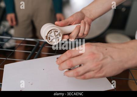 Primo piano di una persona che smonta il prodotto per la rimozione dei pelucchi elettrico per la pulizia, mostra le lame e le pillole di tessuto rimosse su una superficie bianca, concentrandosi sulla casa Foto Stock