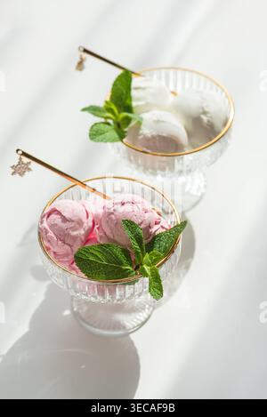 Composizione elegante con due ciotole da dessert in vetro con bordi dorati, ripiene di palline di gelato alla vaniglia e fragole. Foto Stock