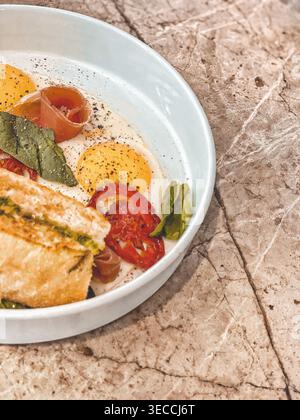 Uova sode soleggiate con pane tostato e verdure sul tavolo, luce calda, colazione Foto Stock