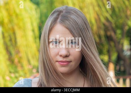 Colpo alla testa di una giovane donna con capelli biondi chiari e occhi blu all'aperto con luce naturale Foto Stock