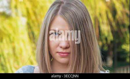 Colpo alla testa di una giovane donna con capelli biondi chiari e occhi blu all'aperto con luce naturale Foto Stock
