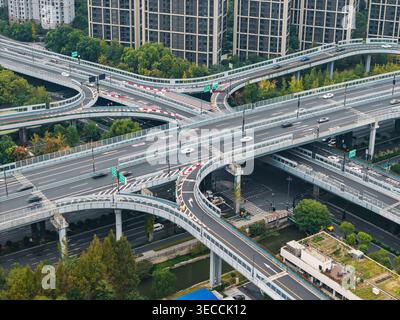 Interscambio autostradale multilivello con numerosi veicoli che attraversano strade sopraelevate e rampe in un ambiente urbano denso Foto Stock