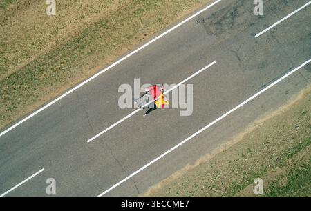 Vista aerea di una coppia di viaggiatori riposano su una strada vuota rettilinea, godendo di tranquillità con le mani dietro la testa Foto Stock