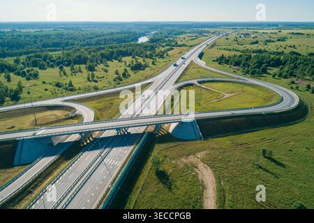 Vista aerea di un moderno svincolo autostradale con più corsie stradali e ponti che si collegano in un vasto paesaggio rurale verde Foto Stock