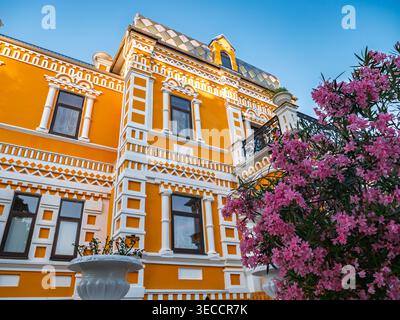 Grande villa arancione che presenta un'architettura elaborata con dettagli decorativi bianchi e un albero in fiore Foto Stock