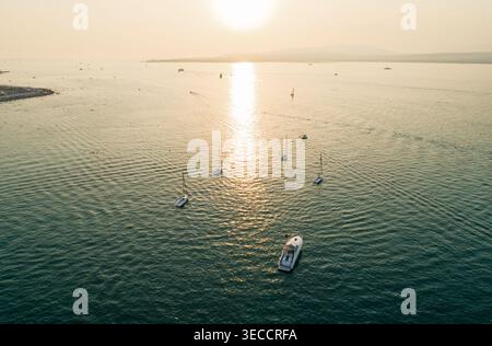 Serena vista del tramonto sull'acqua che mostra più barche a vela e uno yacht a motore che galleggia pacificamente Foto Stock