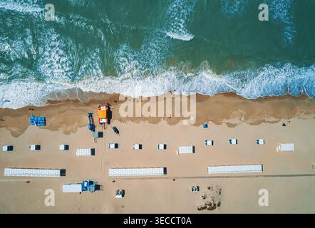 La vista dall'alto mostra un'ampia spiaggia sabbiosa che incontra il profondo blu dell'oceano. Piccole figure di persone camminano vicino all'acqua. Foto Stock