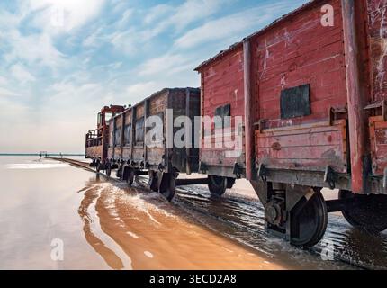 Locomotiva industriale Rusty che traina carri merci in legno attraverso acque rosa poco profonde a Bursol Lake Foto Stock
