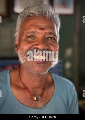 Uomo sorridente con capelli grigi e camicia blu su sfondo rustico, India Foto Stock
