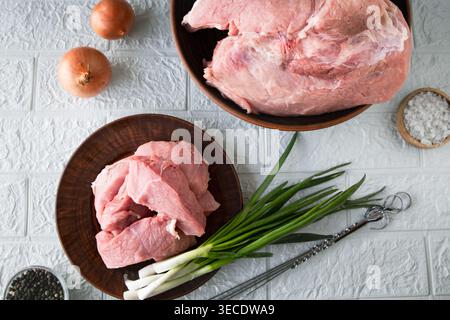 Pezzi di carne di maiale cruda con spezie cipolla e macinacaffè sul tavolo della cucina per la preparazione della cottura Foto Stock