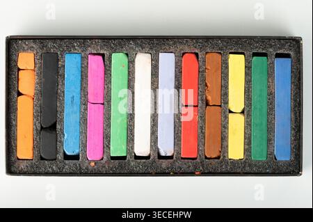 Pezzi di gesso di diversi colori si trovano all'interno di una scatola nera. Sono disposti ordinatamente in fila e mostrano segni d'uso. Foto Stock