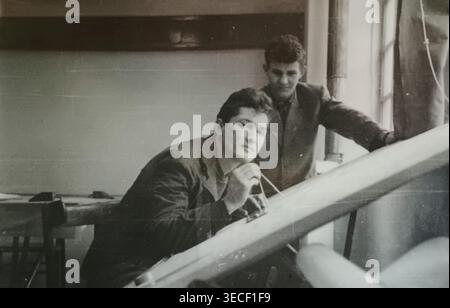 Autentica fotografia d'archivio in bianco e nero di due giovani colleghi che lavorano come disegnatori tecnici (disegnatori) in un cantiere navale di Novi Sad, in Serbia (ex Jugoslavia). L'immagine mostra la precisione del disegno tecnico manuale nell'era pre-digitale, mostrando ai professionisti gli strumenti di disegno su un grande tavolo da disegno. Uno sguardo raro sulla storia industriale e ingegneristica dei Balcani intorno al 1965. Foto Stock