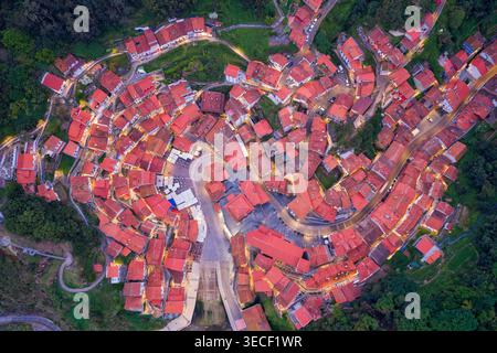 Vista aerea dello storico villaggio di Cudillero con i suoi iconici tetti di tegole rosse e le strade tortuose illuminate da caldi lampioni al crepuscolo di Cudil Foto Stock