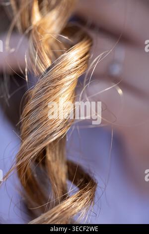 I capelli ricci marrone dorato mostrano una consistenza naturale e i singoli filamenti in una luce soffusa Foto Stock