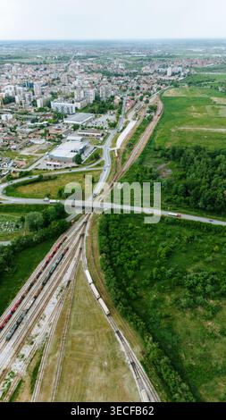 Vista aerea dei treni merci su binari ferroviari vicino a un ponte stradale ed edifici urbani a Sabac, Vojvodina, Serbia. Foto Stock