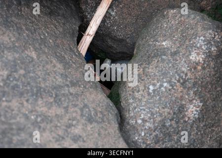 Colpo ad angolo elevato di una bottiglia di plastica e detriti intrappolati in fessure scure di roccia mossy Foto Stock