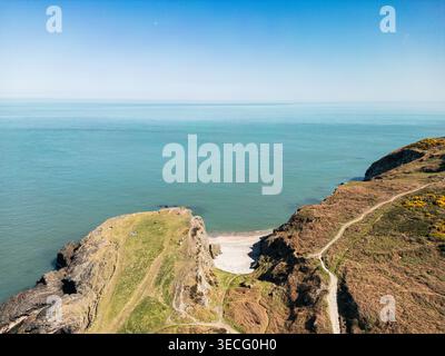 Vista aerea delle scogliere aspre di Wicklow Head e di una spiaggia sabbiosa isolata sotto un cielo azzurro cristallino a Wicklow, nella contea di Wicklow, Irlanda. Foto Stock