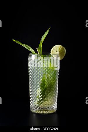 Cocktail di mojito rinfrescante servito in un bicchiere testurizzato con foglie di menta fresca e fetta di lime su sfondo nero. Fotografia in studio minimalista Foto Stock