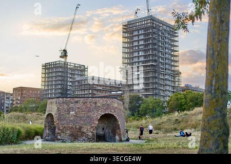Una vista panoramica della rigenerazione urbana a Londra, Regno Unito. In primo piano si erge una struttura industriale storica in mattoni rossi con aperture ad arco, probabilmente un Foto Stock
