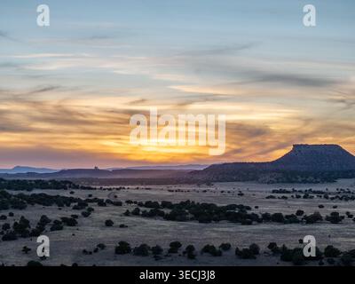 Vista aerea di una mesa dalla cima piatta che si innalza sopra un vasto paesaggio desertico con arbusti e alberi sparsi sotto un colorato cielo al tramonto. Foto Stock