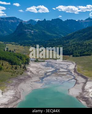 Vista aerea di un lago di montagna turchese con bassi livelli d'acqua che rivelano sponde sabbiose e canali fluviali intrecciati circondati da lussureggianti foreste verdi e da Foto Stock