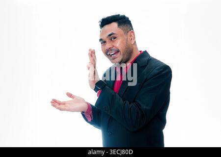Ritratto di un uomo allegro in abito nero e camicia rossa che gesticola con i palmi aperti verso lo spazio per il testo, isolato su sfondo bianco, rappresentante pro Foto Stock