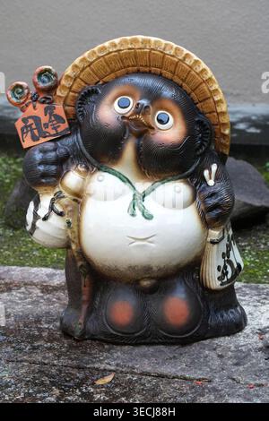 Tradizionale ceramica giapponese Shigaraki Tanuki con indosso un cappello di paglia e una bottiglia di sake, simboleggiando la buona fortuna. Foto Stock