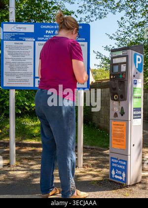 Aprile 2026 - donna vestita in modo informale che usa il suo cellulare per pagare il suo parcheggio nel parcheggio di Church Street a Cheddar, Somerset, Engalnd, Regno Unito. Foto Stock