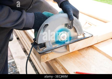 Carpentiere uomo che utilizza una sega circolare per tagliare il legno, chiudere il processo di lavoro. Costruzione di case a telaio, concetto di casa in legno eco-fai-da-te. Operaio qualificato che taglia Foto Stock
