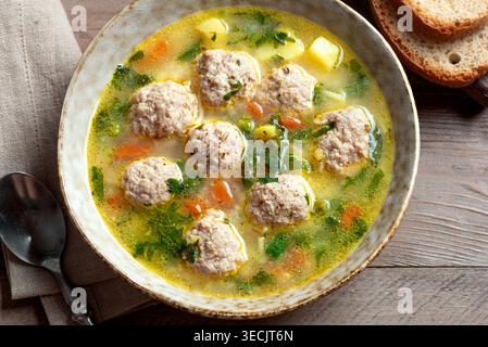 Abbondante zuppa di polpette in ciotola con erbe verdi, primo piano su un tavolo di legno, dettagliato. Zuppa di polpette di pollo fatta in casa con verdure primaverili. Foto Stock