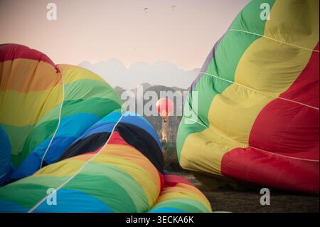 Le colorate mongolfiere si innalzano sopra il nebbioso paesaggio carsico di Vang Vieng, Laos, creando una vibrante scena di volo all'alba con spettacolari montagne e. Foto Stock