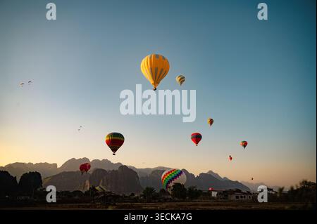 La colorata mongolfiera sorvola un paesaggio panoramico all'alba a Vang Vieng, Laos, con più mongolfiere che fluttuano attraverso un cielo limpido e lontano Foto Stock
