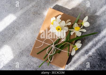 Un'affascinante immagine a tema primaverile con delicati narcisi bianchi legati a una confezione regalo marrone. I fiori simboleggiano il rinnovamento e aggiungono una gioia fresca Foto Stock