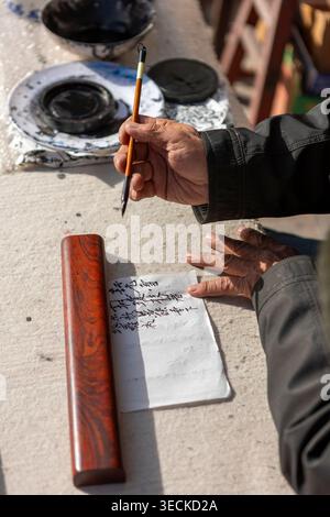 Primo piano di mani anziane che scrivono calligrafia cinese su carta con pennello, pietra d'inchiostro e rotolo, catturando la cultura tradizionale, l'artigianato e la quie Foto Stock