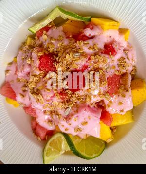 Vista dall'alto di un cestino di frutta colorato con yogurt, muesli, mango, anguria e lime su un piatto bianco, concetto di mangiare sano. Foto Stock
