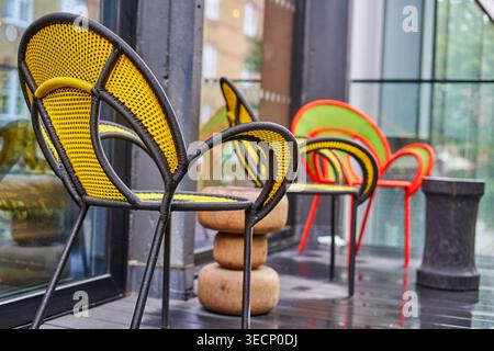 Una vista ravvicinata di sedie moderne colorate disposte su una terrazza o patio bagnato a Londra. Lo sfondo mostra un giallo e nero vivace Foto Stock