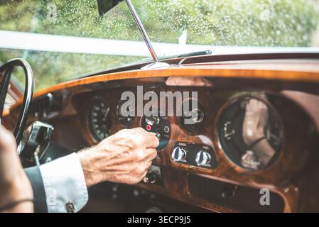 La mano di un uomo gira la chiave di accensione in un'auto d'epoca, pronta ad avviare il motore e a partire per un viaggio Foto Stock