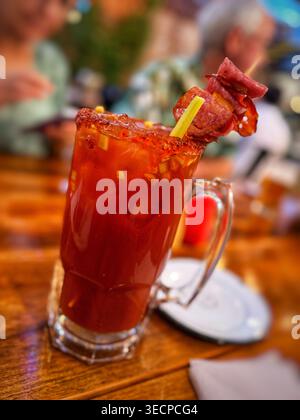 Un rinfrescante cocktail Bloody Mary servito in una tazza di vetro con bordo salato e un elaborato contorno di spiedini di carne e sedano Foto Stock