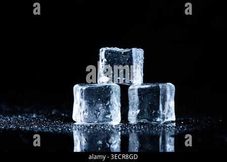 Cubetti di ghiaccio che si fondono in una pila su uno sfondo scuro, mostrando gocce d'acqua e riflessi Foto Stock