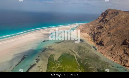 Vista aerea di un'aspra laguna costiera con fondali turchesi, barre di sabbia e scogliere rocciose che incontrano l'oceano blu sotto il cielo nebuloso. Laguna di Detwah, Soko Foto Stock