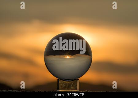 Una sfera di cristallo riflette uno splendido tramonto, catturando i colori vibranti e il caldo bagliore dell'ora d'oro. La tranquilla scena fonde arte e natu Foto Stock