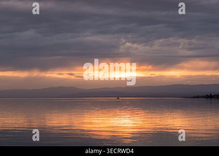 Una vista mozzafiato del sole che tramonta su un tranquillo lago con vivaci tonalità arancio e rosa che illuminano il cielo e l'acqua durante il sereno dorato Foto Stock